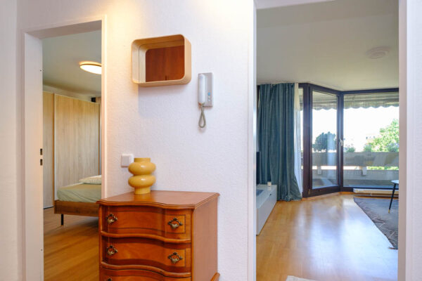 Eingangsbereich mit Kommode und Spiegel. Blick ins Wohnzimmer rechts und Schlafzimmer links